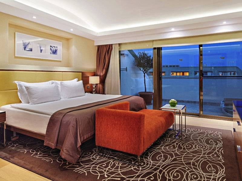 Schlafzimmer im TUI BLUE Side Hotel mit großem Bett, rotem Sessel und Panoramafenstern.