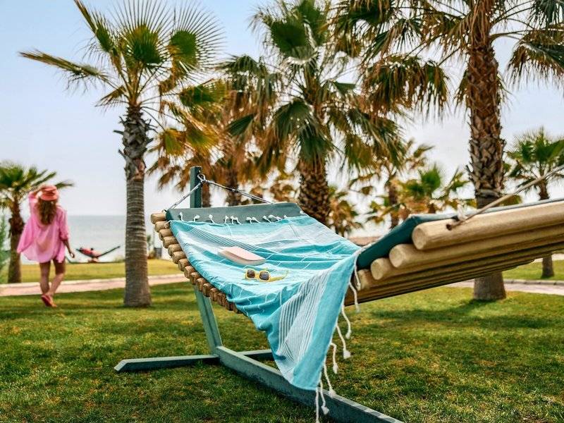 Ein Liegestuhl am Strand des Magic Life Jacaranda Hotels mit einer Person im Hintergrund, die einen Hut und eine Sonnenbrille trägt.