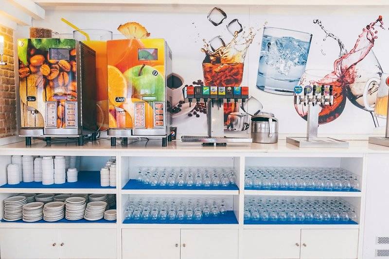 Getränkestation im Calimera Balansat Resort mit Kaffee-, Saft- und Wasserspendern sowie Gläsern und Tellern.