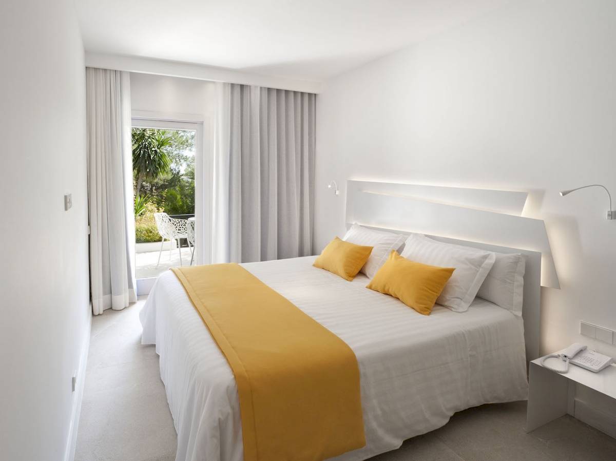 Hotelzimmer im Paraiso de los Pinos mit Bett, gelber Bettdecke, weißem Kopfteil und Zugang zur Terrasse.