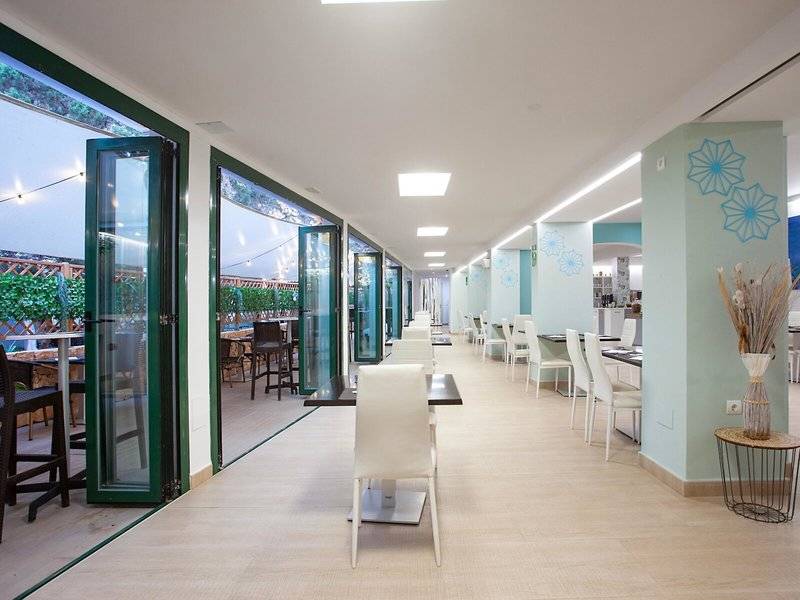 Rosales Formentera Hotelspeisesaal mit weißen Stühlen und Tischen, beleuchteten Decken und großen Fenstern.