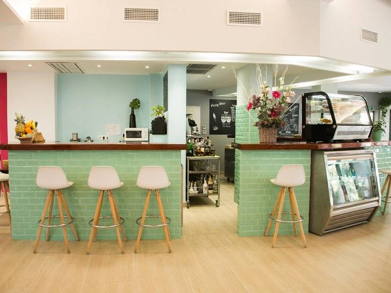 Rosales Formentera Hotel Bar mit grünen Wänden, weißen Stühlen und Obstkorb.