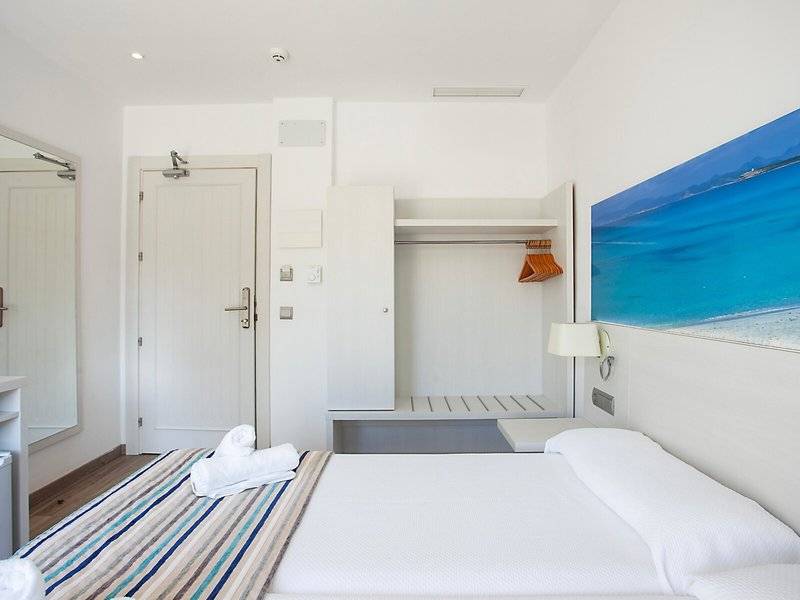 Rosales Formentera Hotelzimmer mit weißem Bett, Decken, Kissen und Badezimmerspiegel.