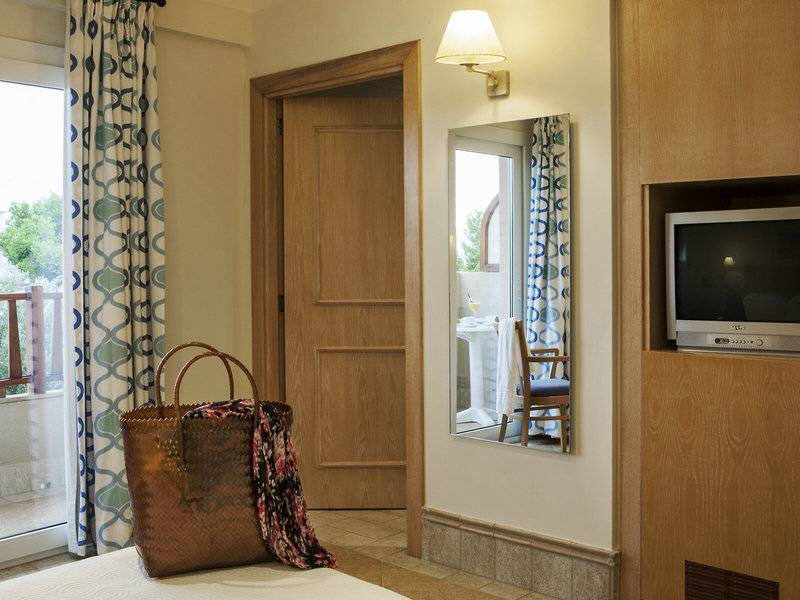 Ein Zimmer im Hotel Voramar Formentera mit einer offenen Tür, einem Spiegel, einem Fernseher und einem Korb auf dem Bett.