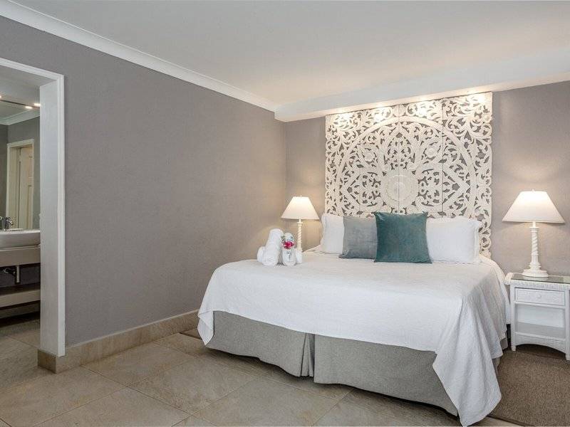 Schlafzimmer im Sugar Bay Barbados Hotel mit weißem Bett, dekorativem Kopfteil und zwei Nachttischen.