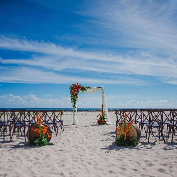 Hochzeitszeremonie auf dem Strand des Hilton Barbados mit Blumenbogen und Stühlen.