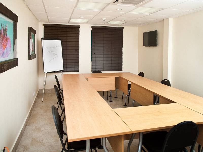 Konferenzraum im Rostrevor Hotel mit langen Holztischen, schwarzen Stühlen, einer Tafel und einer Fernsehwand.