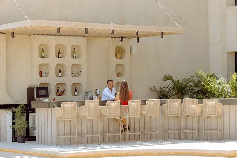 Ein Paar sitzt an der Bar des Sunrise Anjum Resorts, außen vor einer Wand mit Flaschen und Pflanzen.