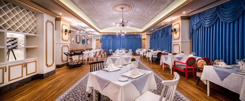 Innenansicht des Restaurants im Sensitive Premium Resort & Spa, mit gedeckten Tischen, blauen Vorhängen und Holzboden.