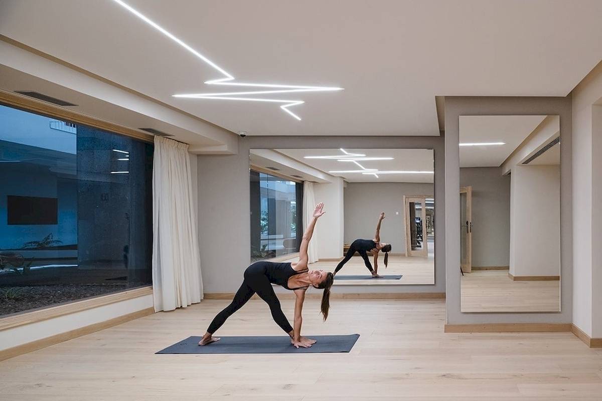 Yogaraum im Plus Fariones Suite Hotel mit zwei Frauen, die Yoga praktizieren, vor großen Fenstern.