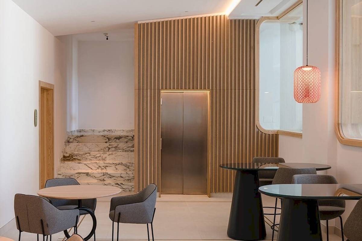 Innenansicht der Lobby im Plus Fariones Suite Hotel mit Marmortreppen, braunen Holzwänden und modernen Möbeln.