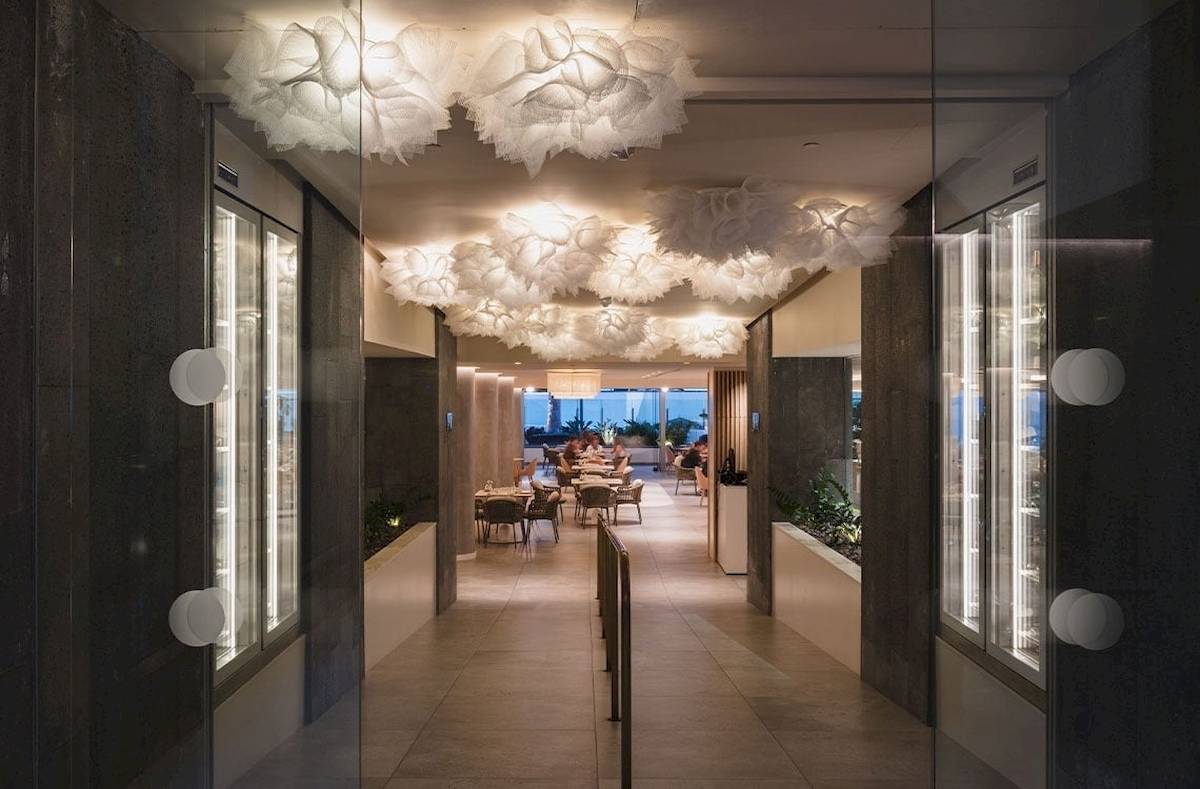 Innenbereich des Plus Fariones Suite Hotels mit geometrischen Deckenleuchten und Tischen im Freien.