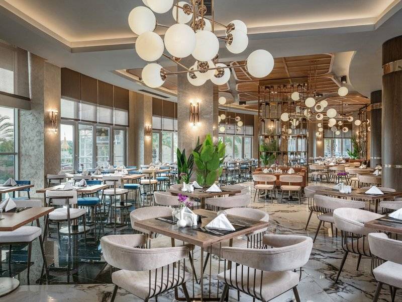 Innenbereich des Restaurants im Kirman Leodikya Resort mit modernen Möbeln, hängenden Kronleuchtern und großen Fenstern.