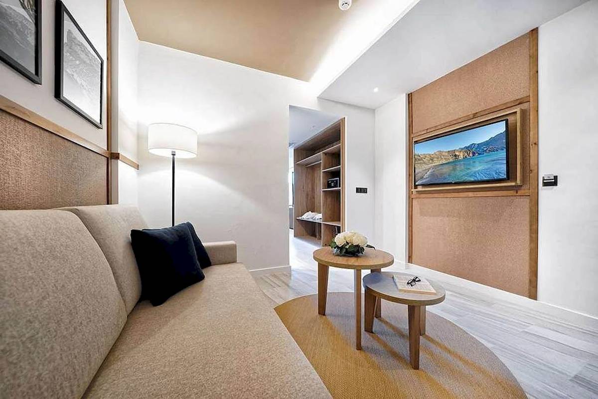 Innenbereich des H10 Costa Mogan Hotels mit Wohnzimmer, Couch, Tisch, Fernseher und Lampe.