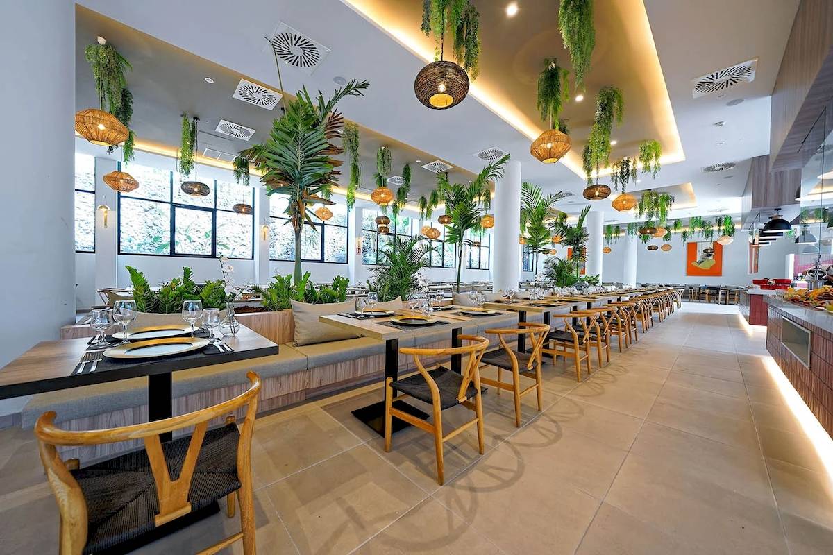 Innenansicht des Restaurants im H10 Costa Mogan Hotel mit hängenden Pflanzen und gedeckten Tischen.