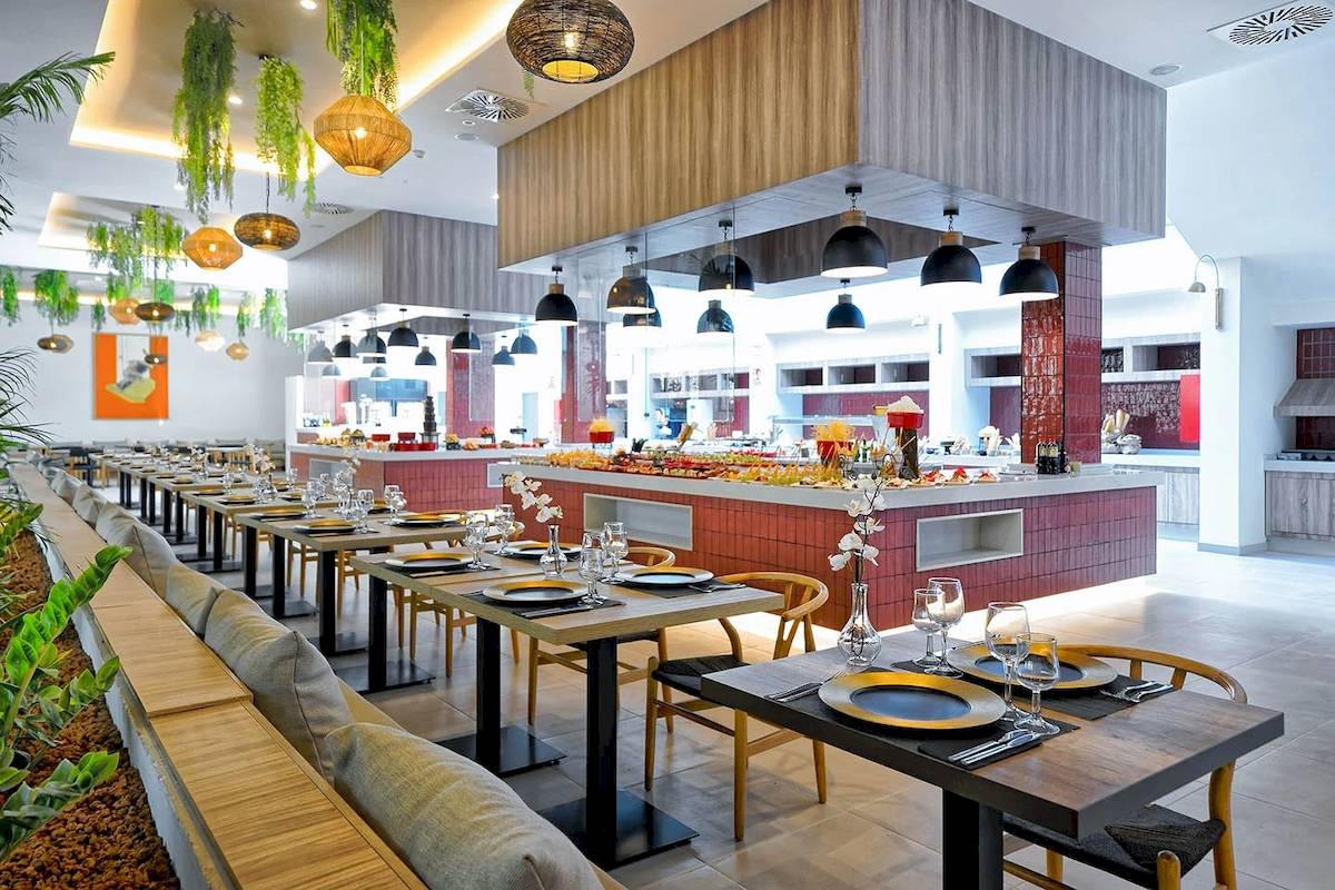 Innenbereich des H10 Costa Mogan Hotels mit Tisch, Stühlen und Speisenbuffet.