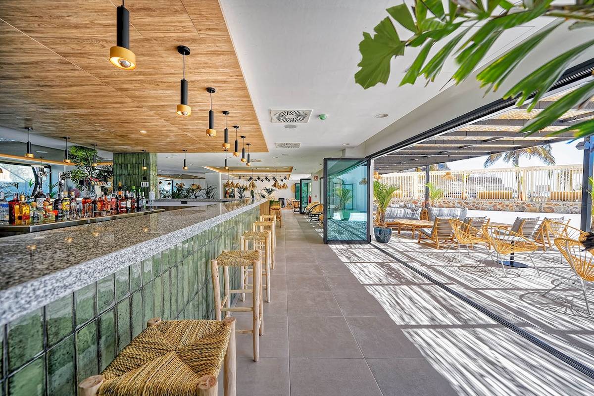 Innenansicht der Bar im H10 Costa Mogan Hotel mit grünen Wänden und Holzmöbeln.