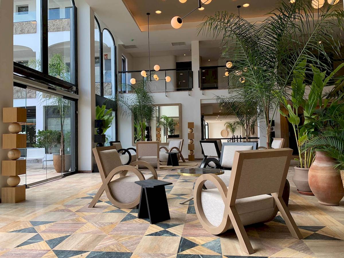 Lobby des H10 Costa Mogan Hotels mit moderner Einrichtung, geometrischem Bodendesign, großen Pflanzen und stilvollen Möbeln.