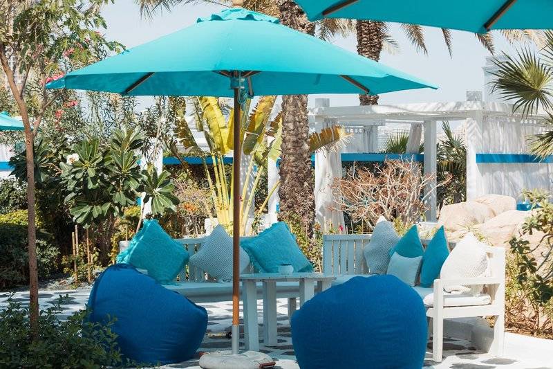 Lounge-Bereich des W Dubai - Mina Seyahi Hotels mit blauen Kissen, Sesseln und Sonnenschirmen.