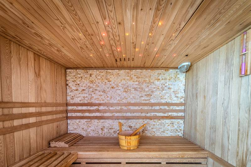 Eine Holzsauna mit einem Holzbecken und einer beleuchteten Decke.