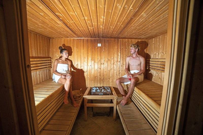 Eine Frau und ein Mann sitzen in einer Holzsauna im VOI Baia di Tindari Resort.