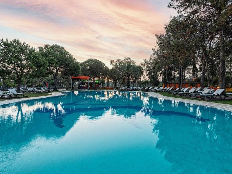 Am Abendaufnahme des Infinity-Pools im Megasaray Resort Side mit Sonnenliegen und Bäumen.