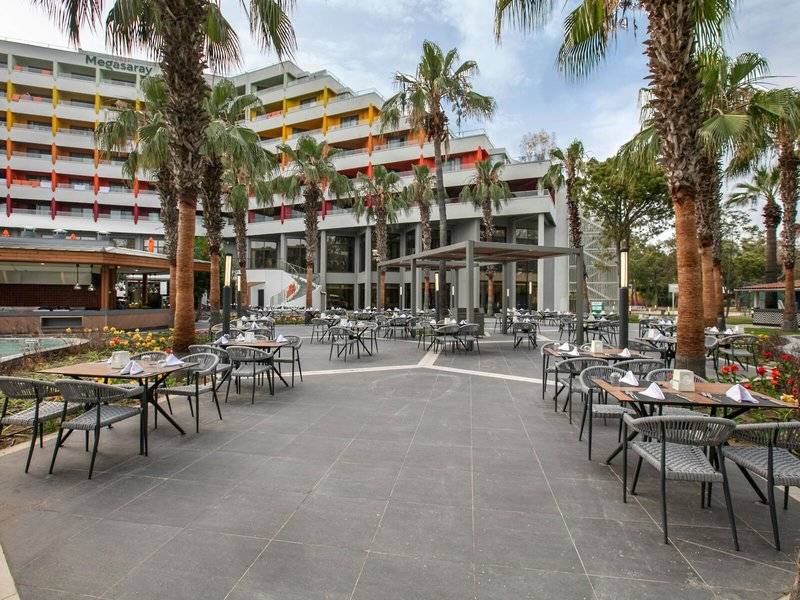 Außenbereich des Megasaray Resort Side mit mehreren Tischen und Stühlen unter Palmen.
