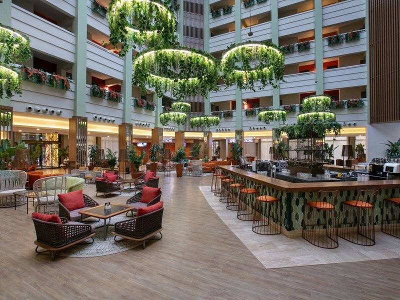 Lobby des Megasaray Resort Side mit Sitzgelegenheiten, Bar und begrünten Deckenleuchten.