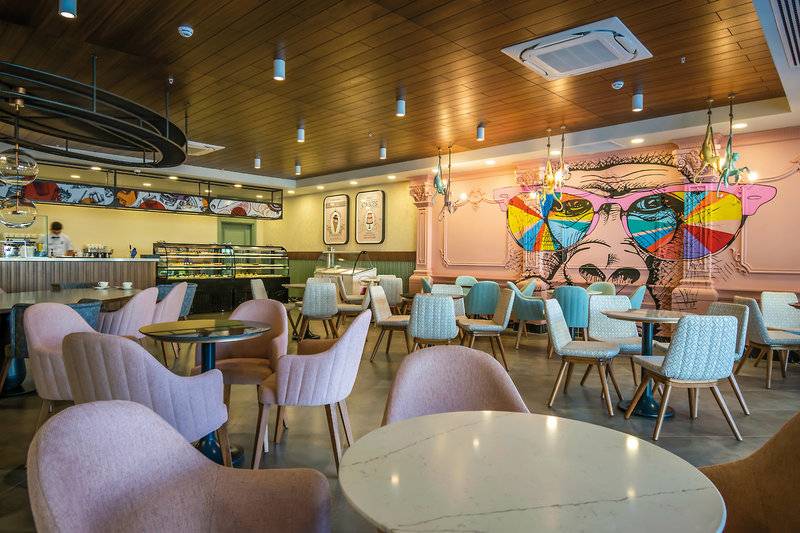Innenbereich des Restaurants im Seaden Quality Resort & Spa mit bunten Wänden und runden Tischen.
