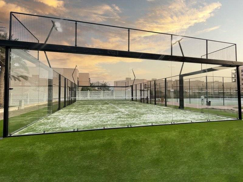 Tennisplatz im Intercontinental Doha Beach & Spa Hotel, eingezäunt mit Glaswänden und grünem Kunstrasen.