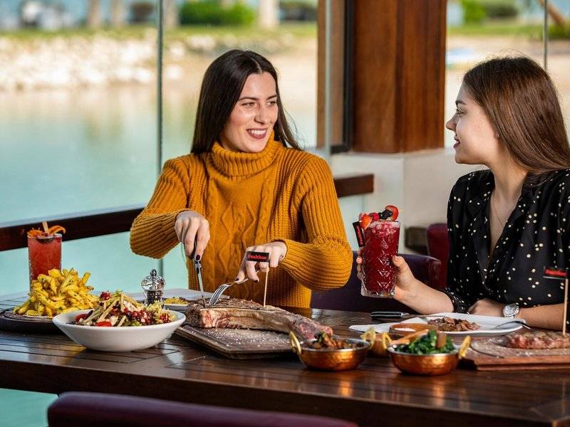 Zwei Frauen essen im Sheraton Doha Resort Convention Hotel mit Blick auf den See.