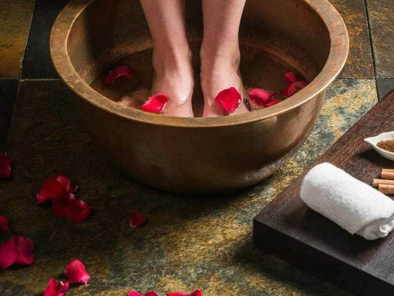 Füße in einem Holzbecken mit Rosenblättern und Gewürzen, nahe eines Handtuchs