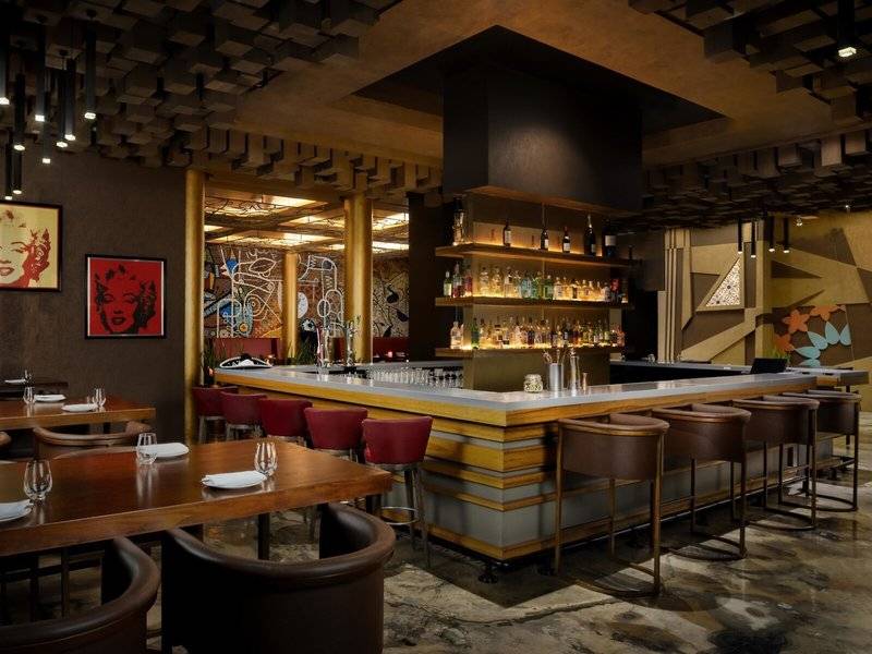 Innenansicht der Bar im Marsa Malaz Kempinski, The Pearl mit gepolsterten Stühlen und einer Theke mit vielen Flaschen.