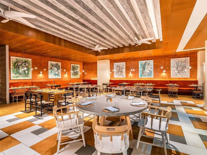 Innenbereich des Restaurants im Rixos Gulf Hotel Doha mit runden Tischen und Stühlen.