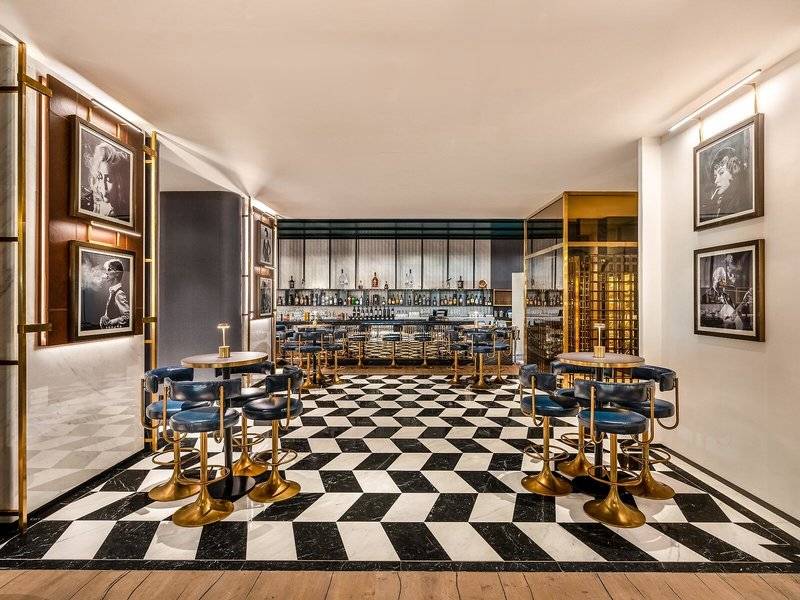 Innenbereich der Bar im Rixos Gulf Hotel Doha mit schwarzen und weißen Schachbrettboden und goldenen Stühlen.
