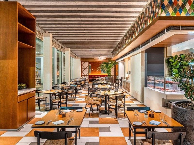 Innenansicht des Restaurants im Rixos Gulf Hotel Doha mit geometrischen Bodenfliesen und Holzmöbeln.