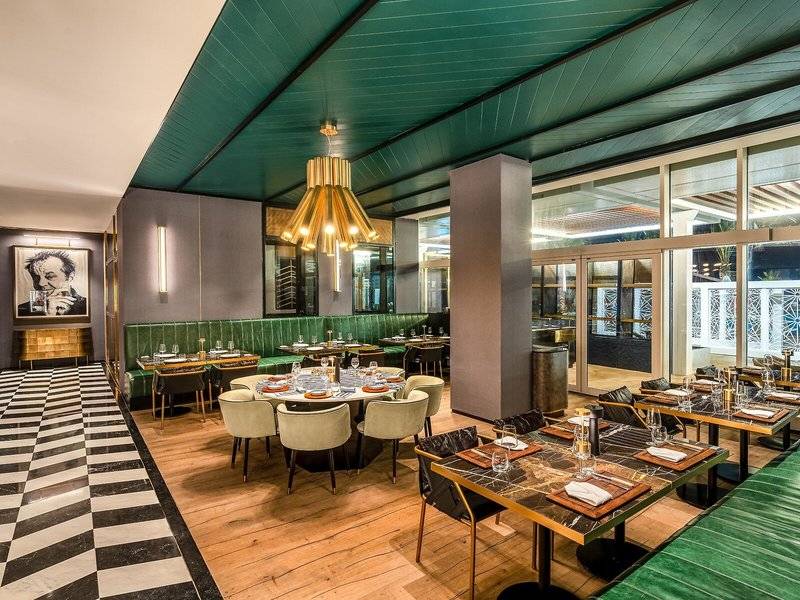 Innenbereich des Rixos Gulf Hotel Doha mit grüner Decke, grünen Sofas und Marmortischen.