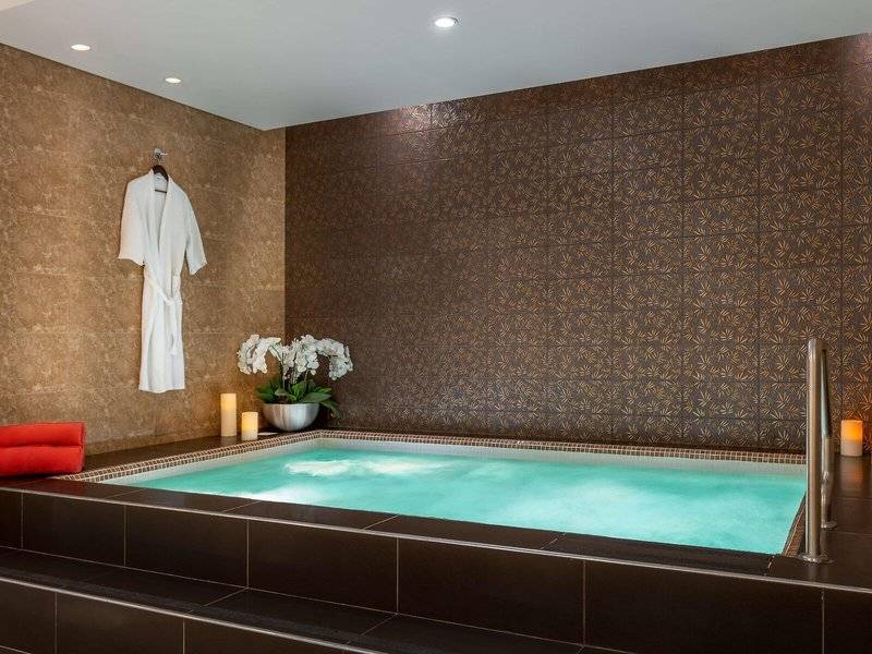 Jacuzzi im Badezimmer des Hyatt Regency Oryx Doha mit braunen Wänden, weißen Fliesen und Blumenvase.