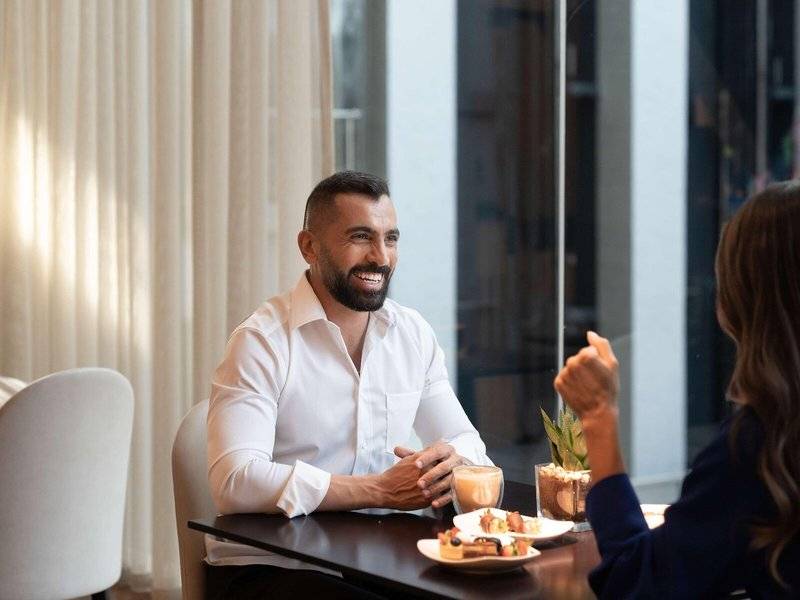 Ein Mann und eine Frau sitzen im Restaurant des Hyatt Regency Oryx Doha, lächeln und unterhalten sich.