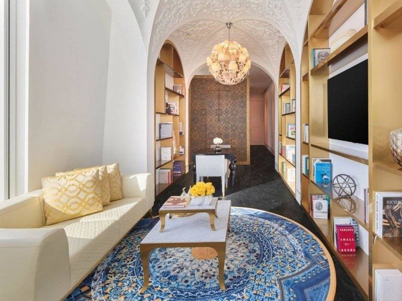 Innenansicht des Wohnzimmers im Raffles Doha mit weißem Sofa, goldenem Tisch, blauem Teppich und Bücherregalen.