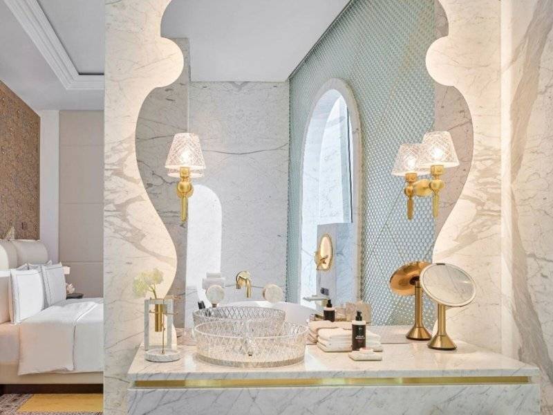 Das Badezimmer des Raffles Doha Hotels mit weißem Marmor und goldenen Details.