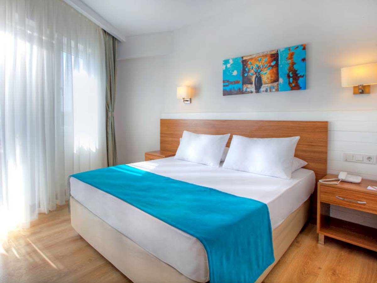 Schlafzimmer im Grand Park Lara Hotel mit blauer Bettdecke und weißen Kissen auf einem Bett mit Kopfteil.