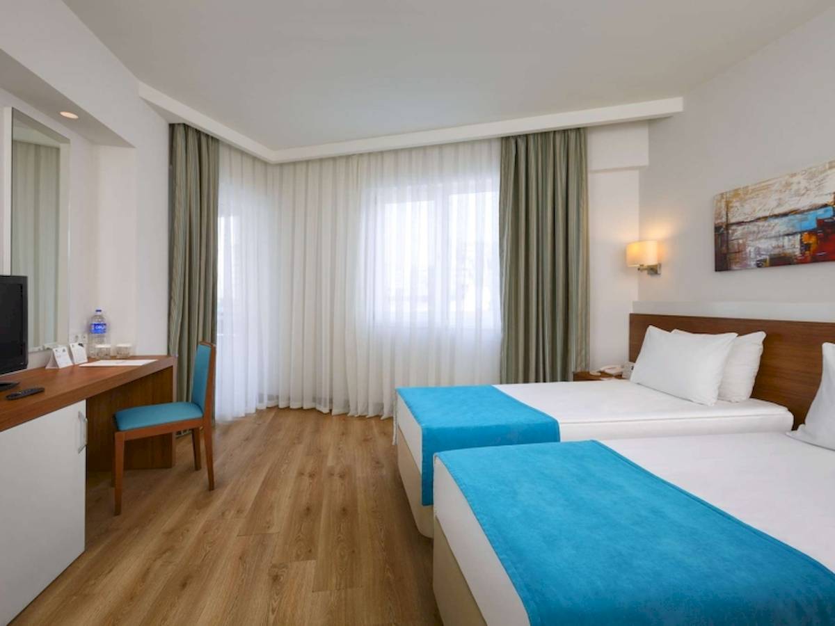 Innenansicht eines Hotelzimmers im Grand Park Lara Hotel mit zwei Betten, Schreibtisch und Fernseher.