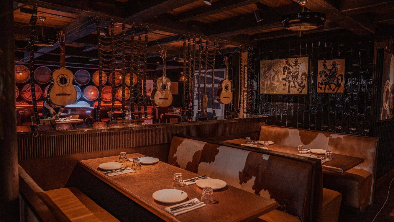 Innenraum des St. Regis Doha mit dunklen Wänden, Holzbänken, aufgehängten Gitarren und Gemälden.