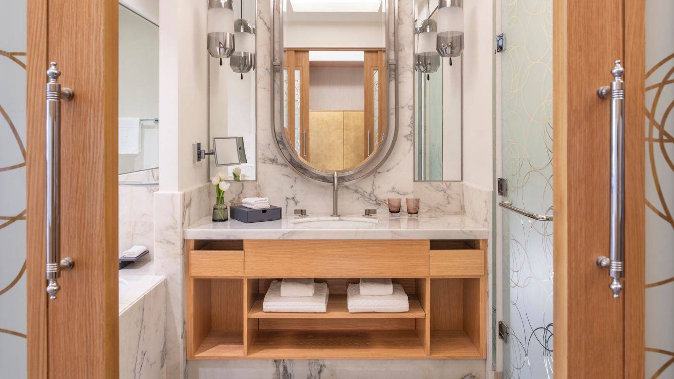 Badezimmer im St. Regis Doha mit Marmorboden, Waschbecken, Spiegel und Holzschränken.