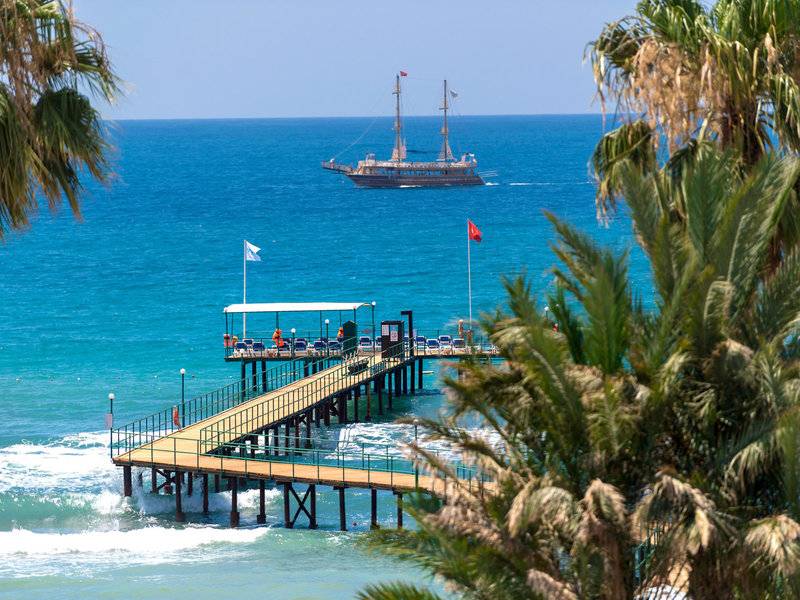 Turquoise Hotel Pier mit einem Boot im Hintergrund, umgeben von Palmen und Wasser.