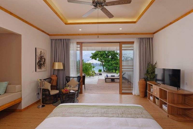 Innenansicht des Schlafzimmers im Brenneri Kottefaru Maldives mit offenem Fenster, Blick auf den Strand und modernen Möbeln.