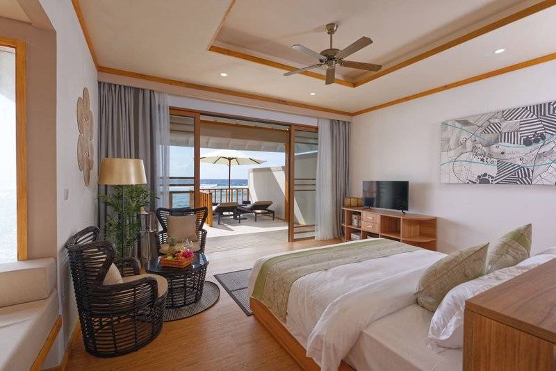 Innenansicht einer Suite im Brennia Kottefaru Maldives mit Meerblick, Bett, Möbeln und Fernseher.