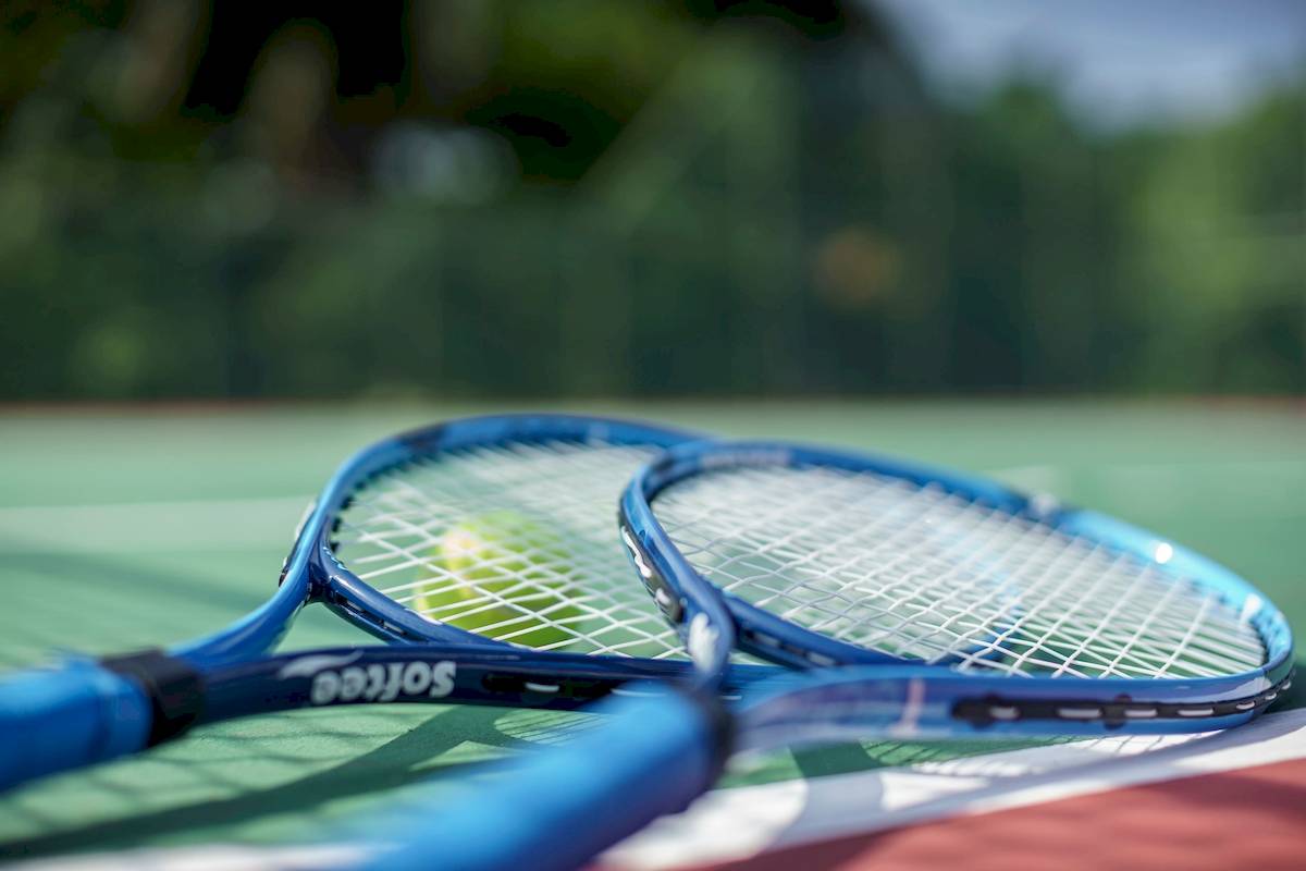 Tennisschläger auf einem Tennisplatz mit einem Tennisball im Hintergrund.