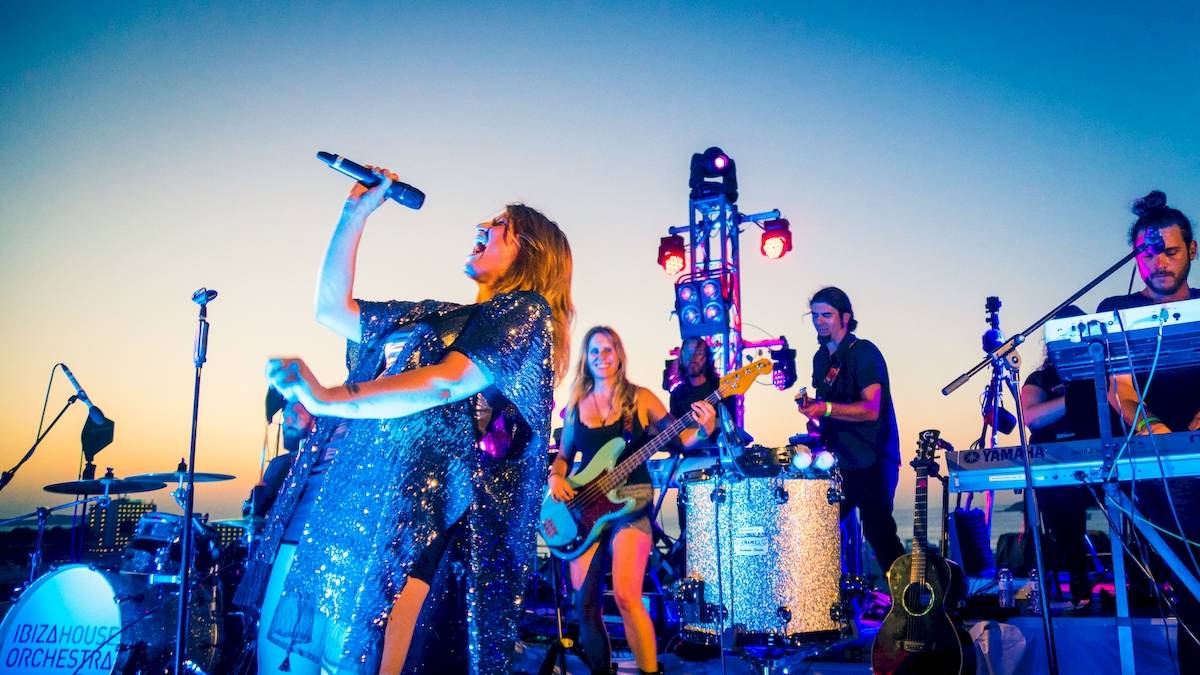 Ibizahouse Orchester Auftritt bei Sonnenuntergang mit Sängerin, Gitarristen und Schlagzeugern.